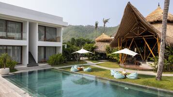 A modern resort with a swimming pool, a thatched-roof structure, and a white building with balconies.