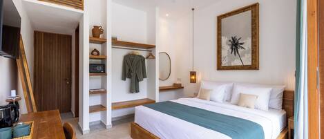 A bedroom with a bed, bedside table, and a mirror. There is a wooden bench and a small table with a tray.