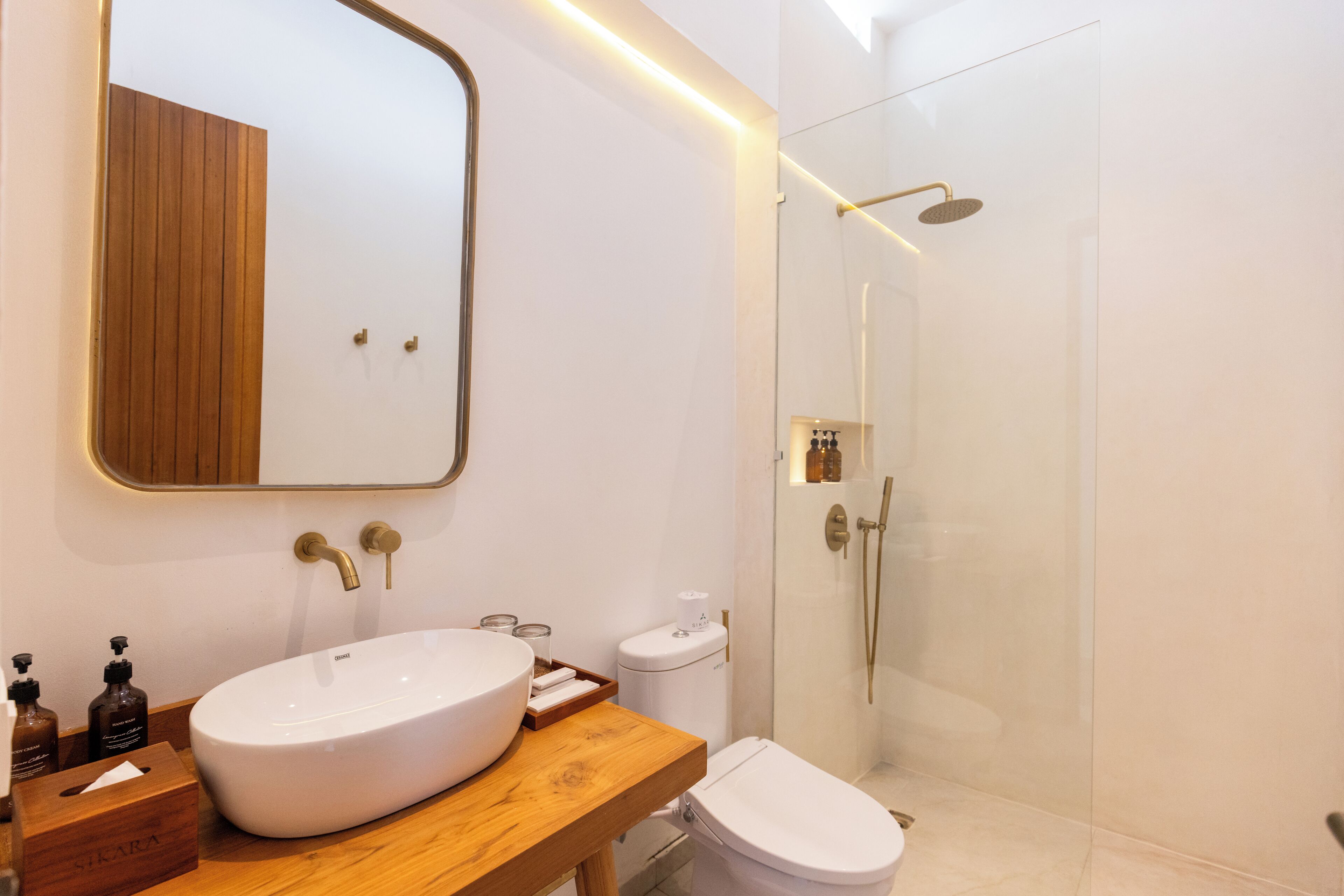 A modern bathroom with a wooden vanity, a large white sink, a toilet, and a glass-enclosed shower area.
