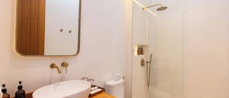 A modern bathroom with a wooden vanity, a large white sink, a toilet, and a glass-enclosed shower area.