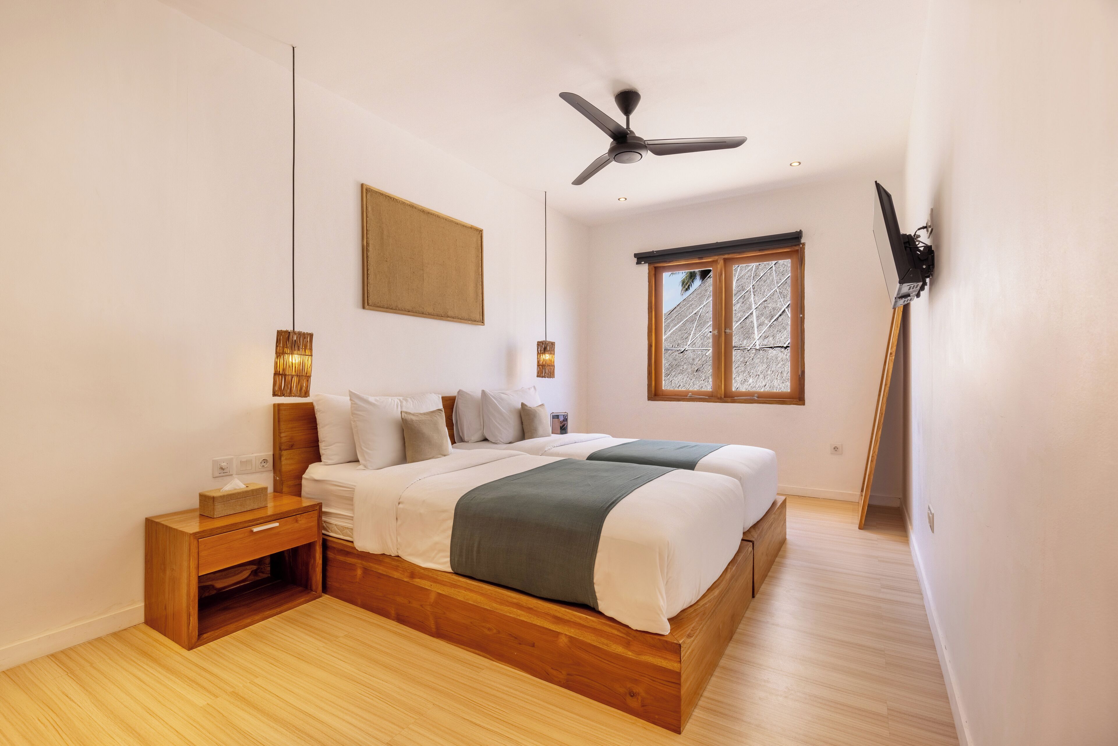 A bedroom with two beds, a ceiling fan, a window, and a wooden nightstand.