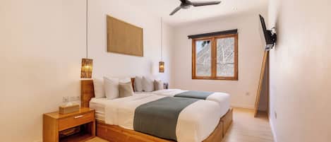 Un dormitorio con dos camas, un ventilador de techo, una ventana y una mesita de noche de madera.
