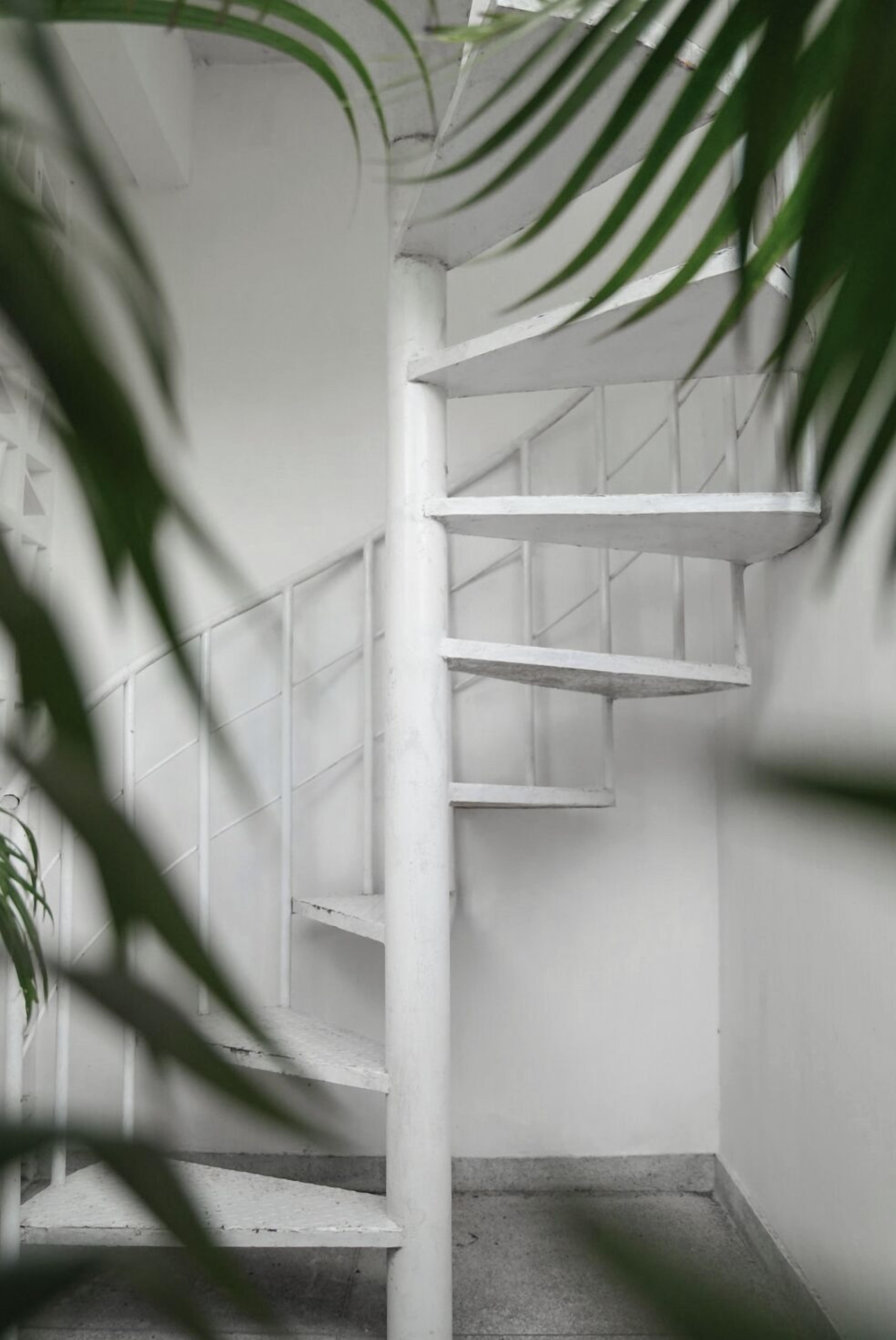 A white spiral staircase in a corner with a concrete floor.