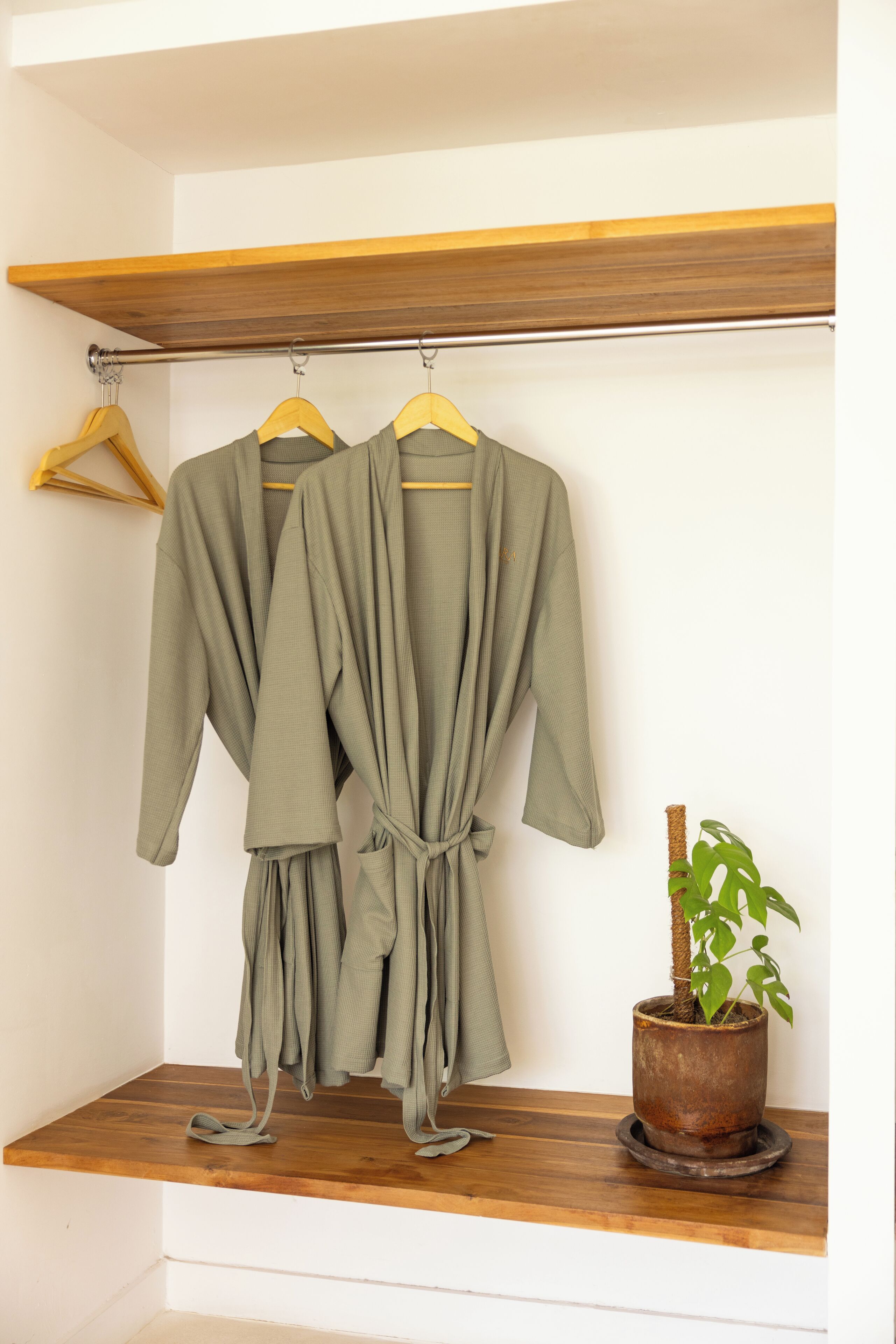 A wooden shelf with two green robes hanging on a metal rod, a potted plant, and a wooden bench.