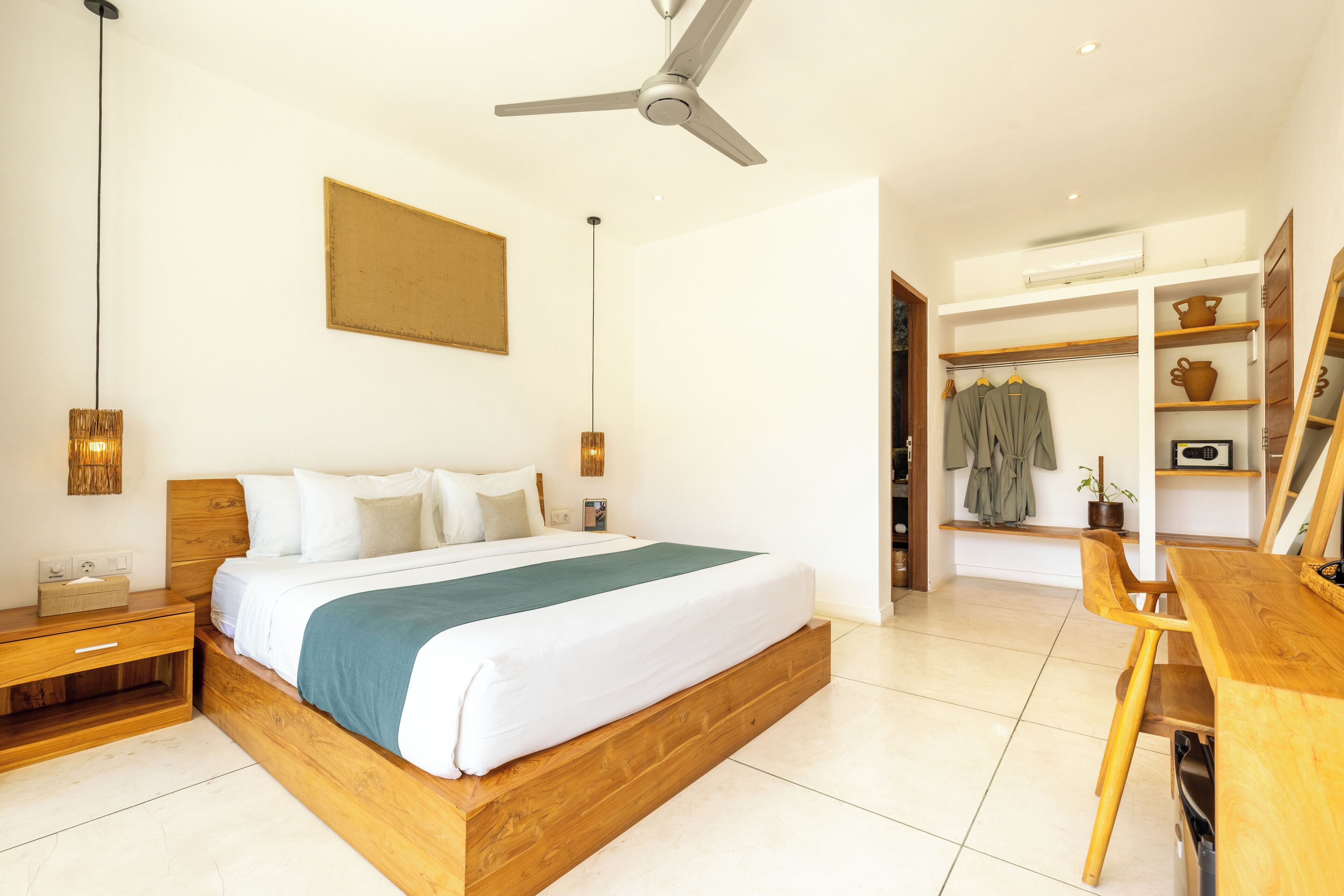 Ein modernes Schlafzimmer mit einem Holzbett, Nachttischen, einem Deckenventilator und Blick in einen angrenzenden Wohnbereich mit Schreibtisch und Regalen.