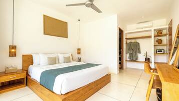 Une chambre moderne avec un lit en bois, des tables de chevet, un ventilateur de plafond et une vue sur un espace de vie attenant, comprenant un bureau et des étagères en bois.