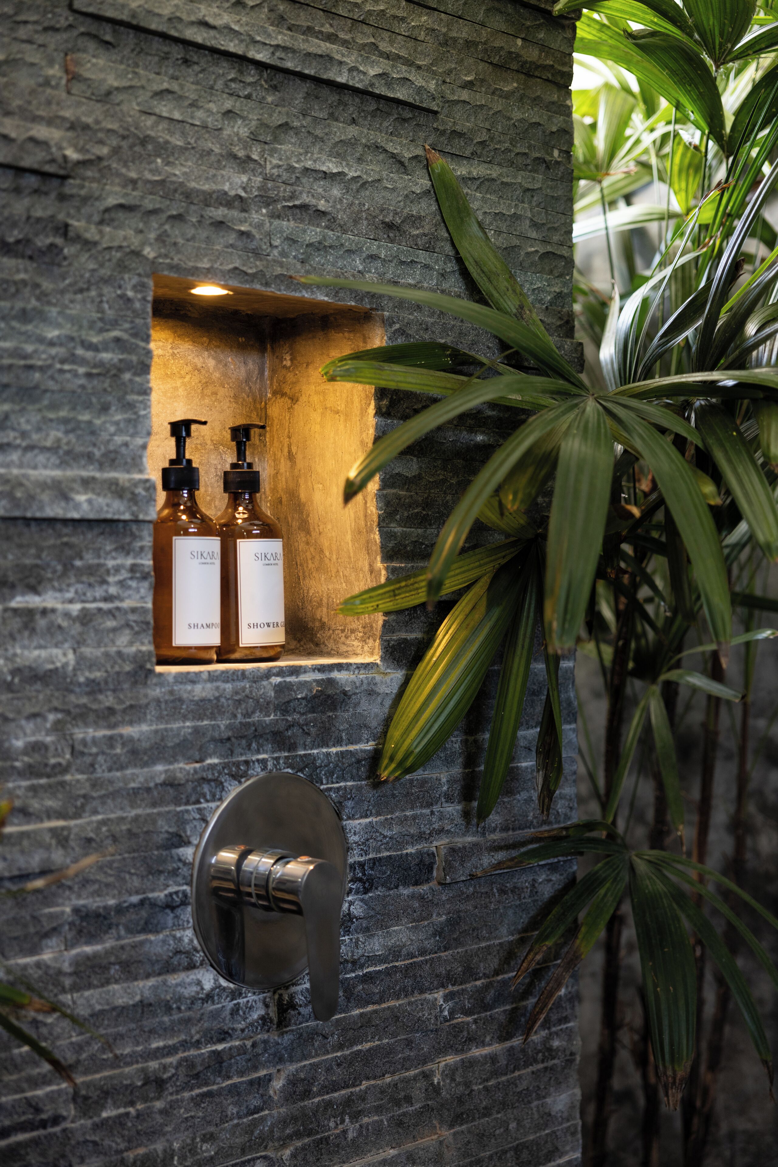 A stone wall with two bottles of shampoo and shower gel, and a modern faucet.