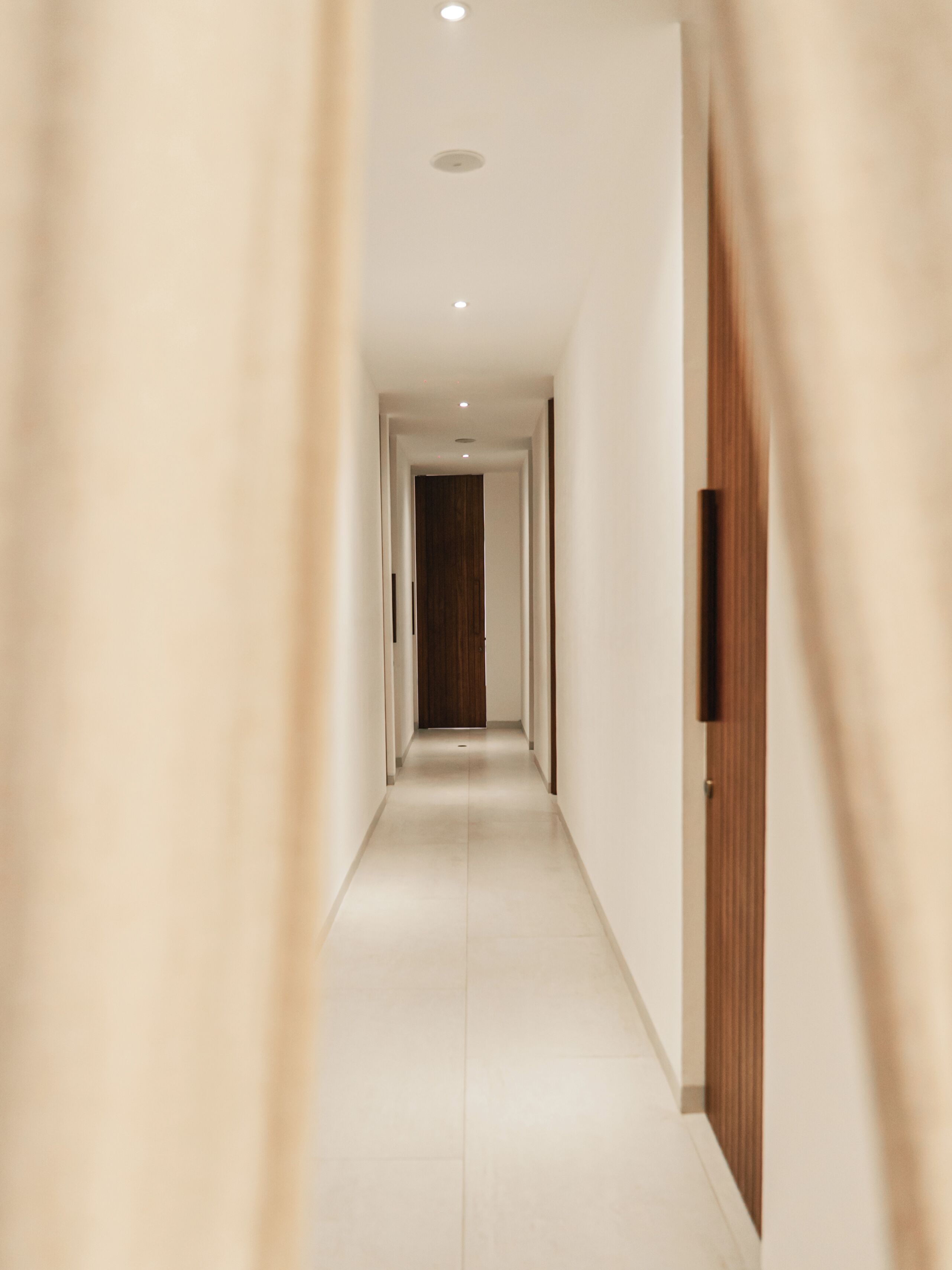 Um corredor com uma porta de madeira no final, dando acesso a um quarto.