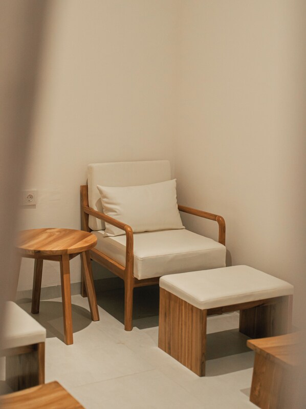 A minimalist room with a wooden chair, a small round table, and a matching ottoman. - Sikara Lombok Hotel (Kuta)
