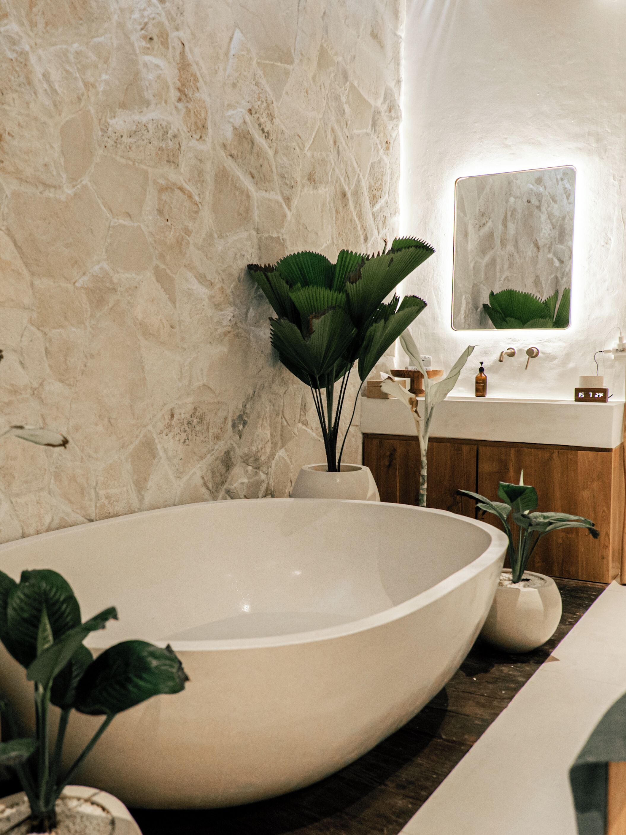 Une salle de bain avec un grand lavabo blanc, un miroir et un mur en pierre.