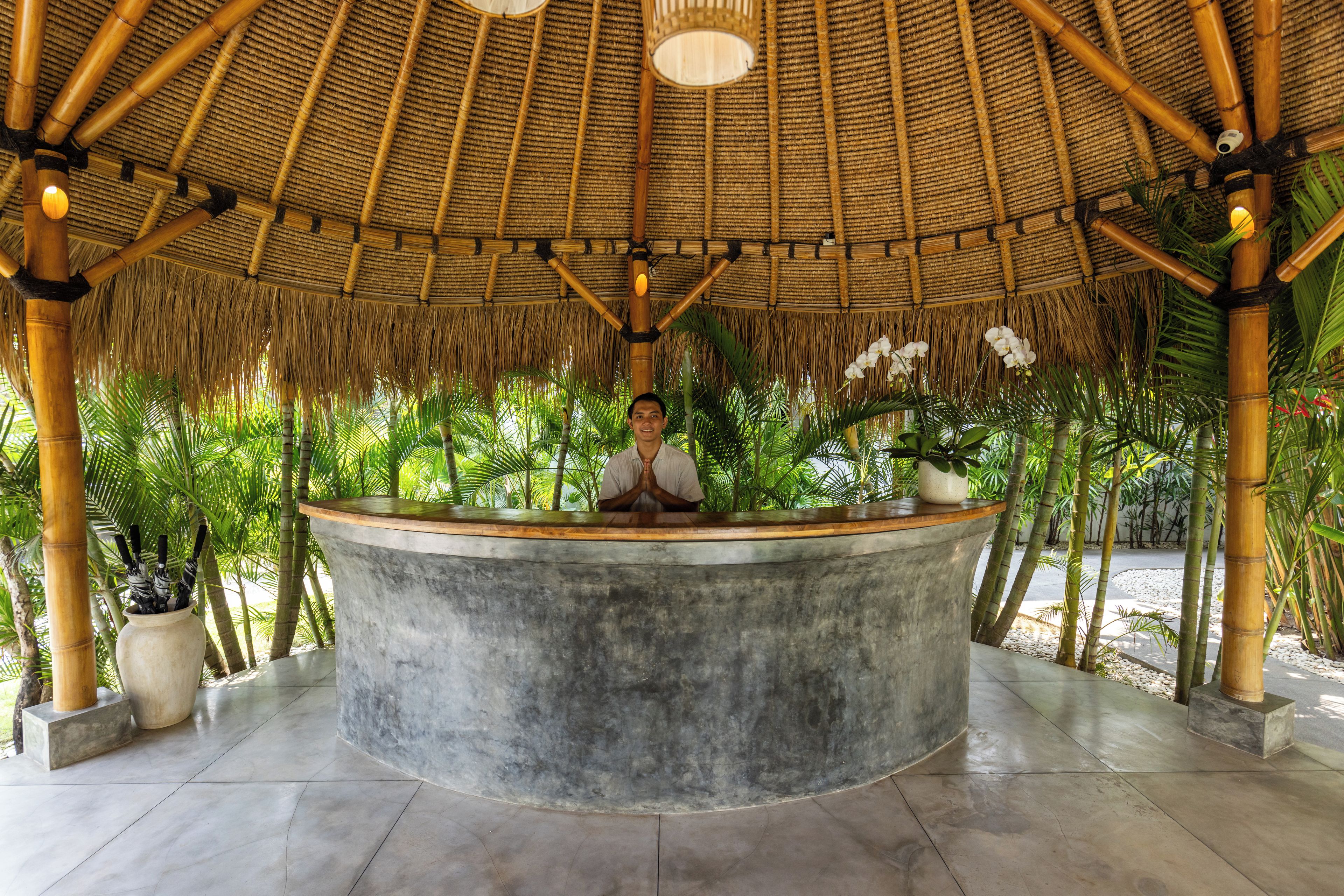 A reception area with a curved concrete counter, a thatched roof, and a person standing behind it.