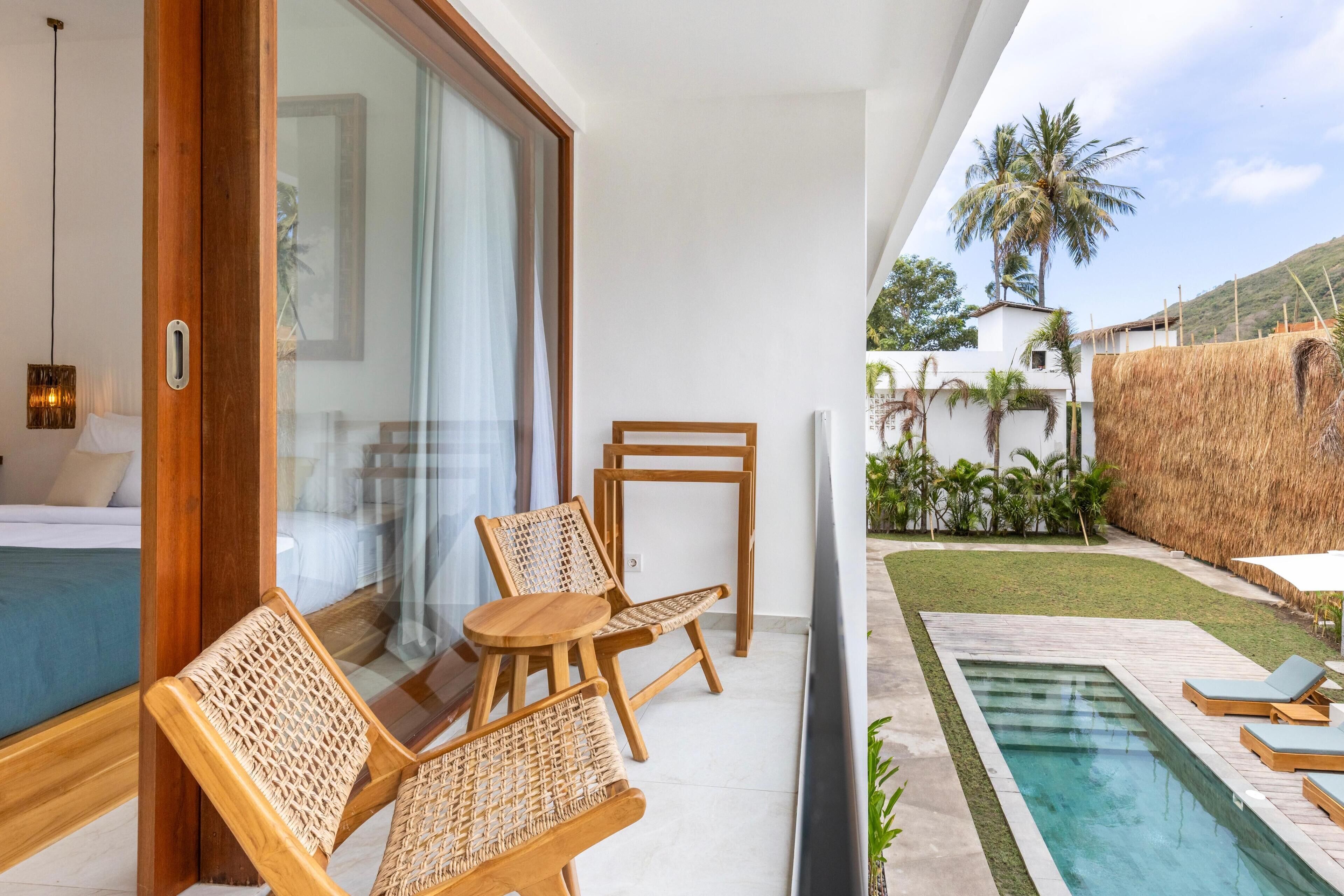 Un área exterior moderna con piscina, mobiliario de madera y vistas a un exuberante jardín con palmeras.