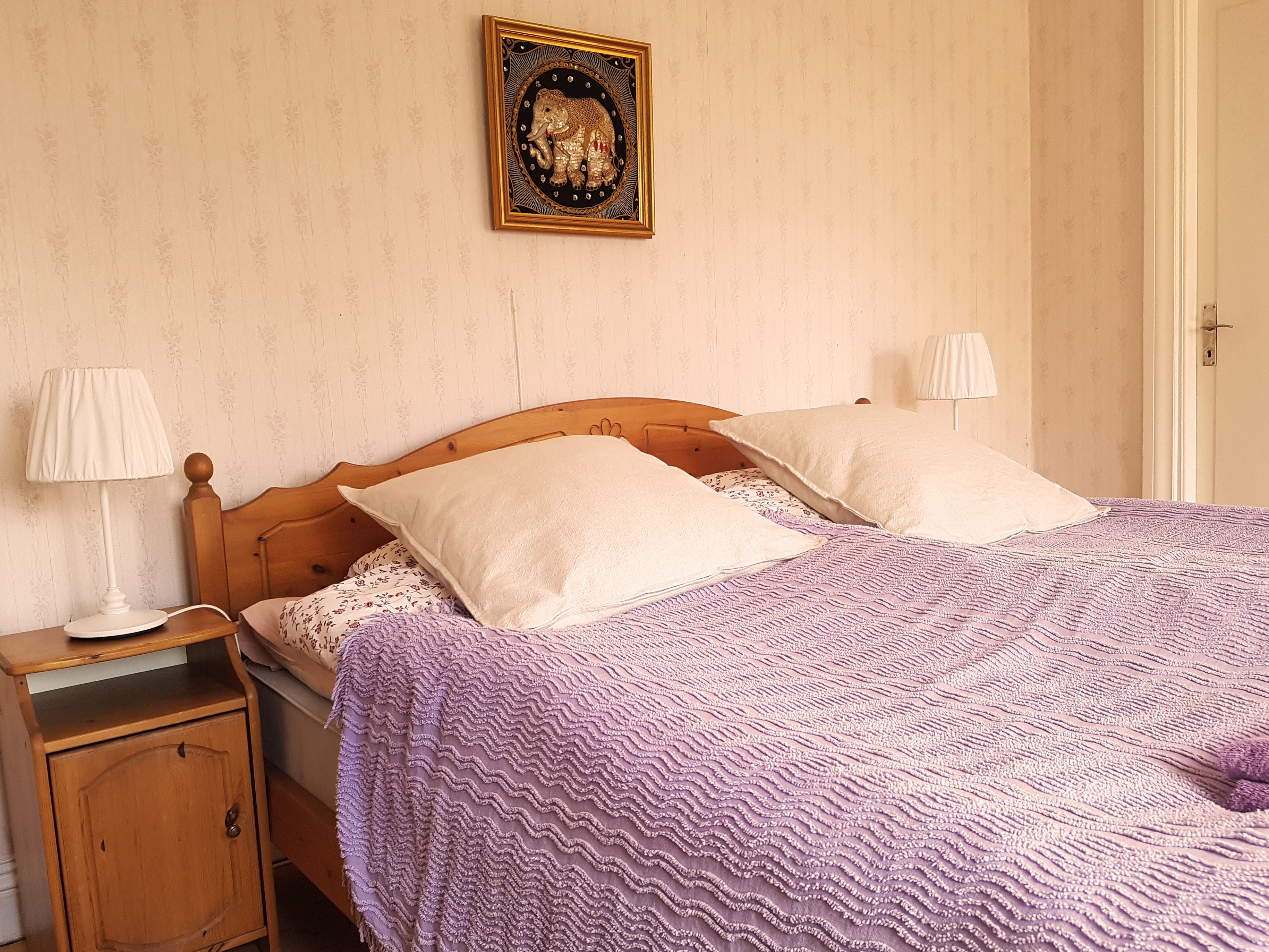 Un dormitorio con una cama de madera, dos lámparas de noche, una mesita de noche, un armario y un cuadro enmarcado en la pared.