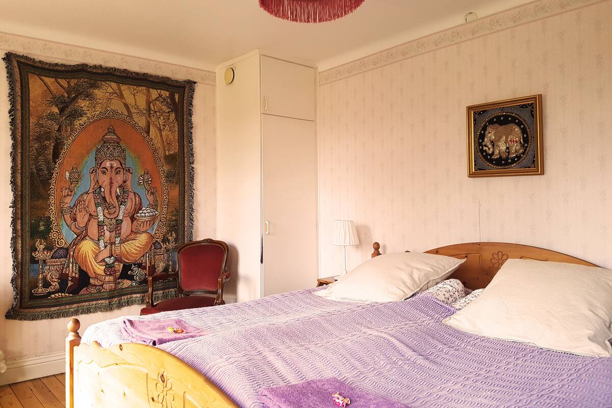 A bedroom with a bed, a tapestry, a chair, and a wall-mounted picture.