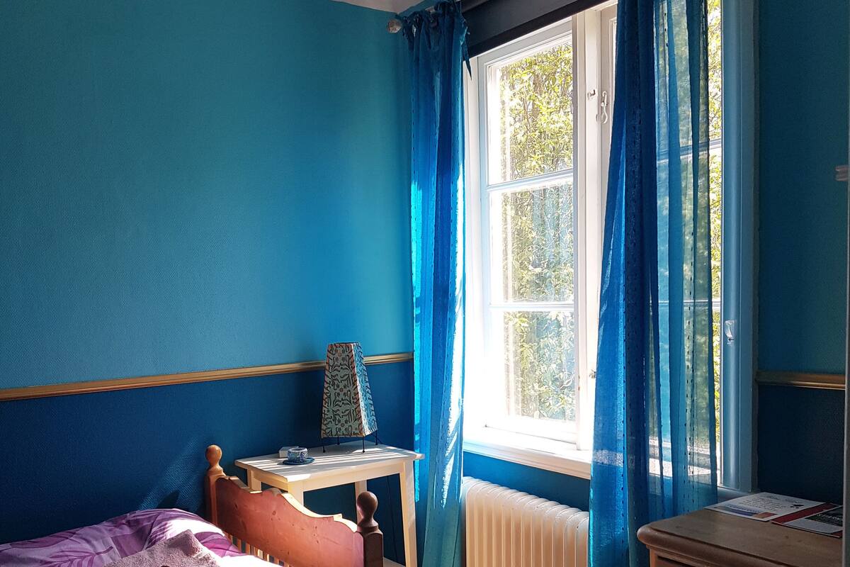A bedroom with a bed, a desk, a dresser, and a window with curtains.