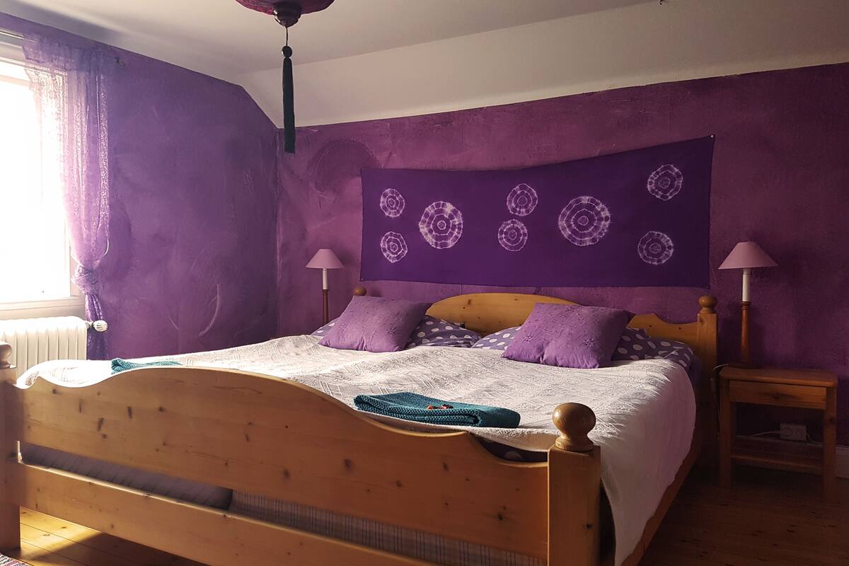 A bedroom with a wooden bed, purple walls, and a ceiling fan.