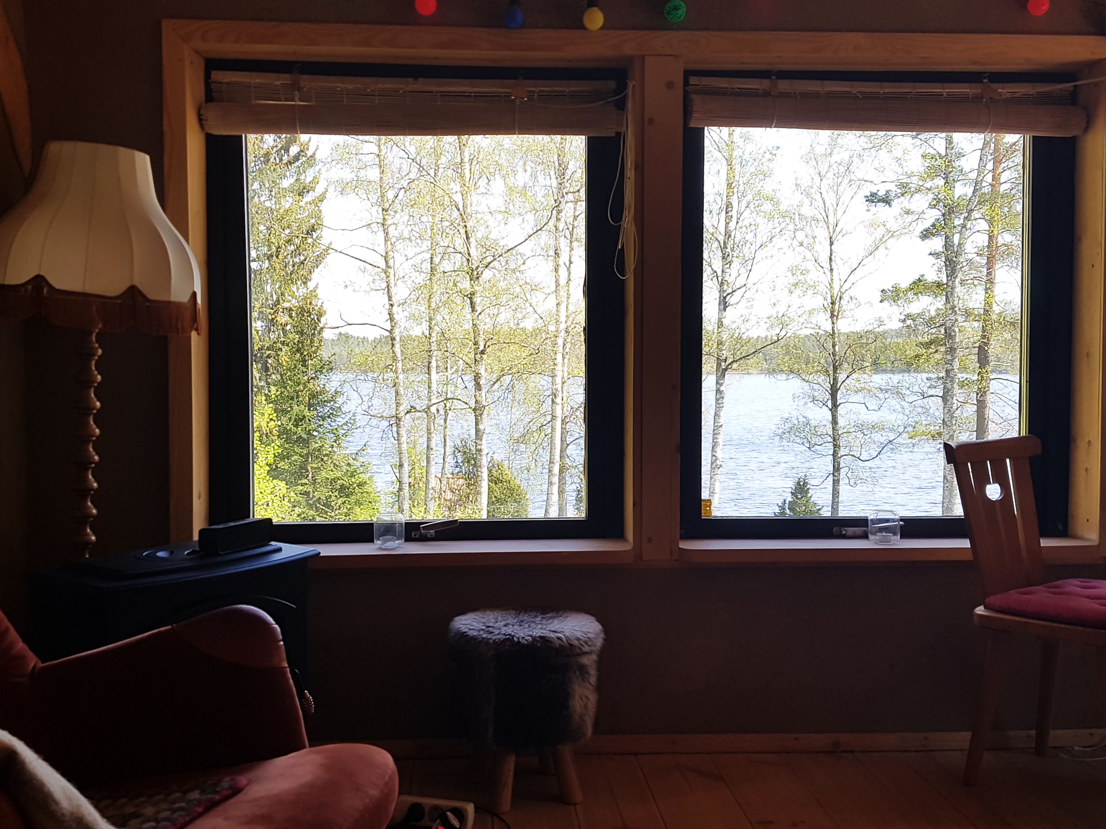 Una habitación con dos ventanas que dan a un lago, una lámpara, una silla y un taburete pequeño.