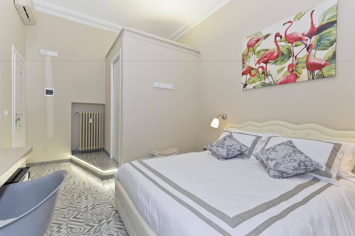Une chambre d’hôtel avec un lit, une chaise, un radiateur et un tableau représentant des flamants roses.