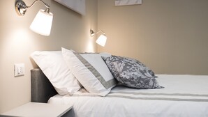 A neatly made bed with white and gray bedding, two wall-mounted reading lamps, and a small bedside table. - B&B Tohouse Deluxe (Turin)