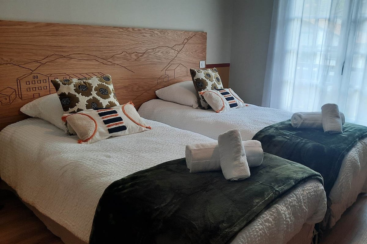 A hotel room with two beds, each with a headboard, multiple pillows, and a blanket.