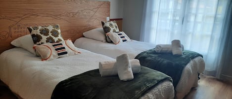 Habitación de hotel con dos camas, cada una con cabecero, varios almohadones y una manta.