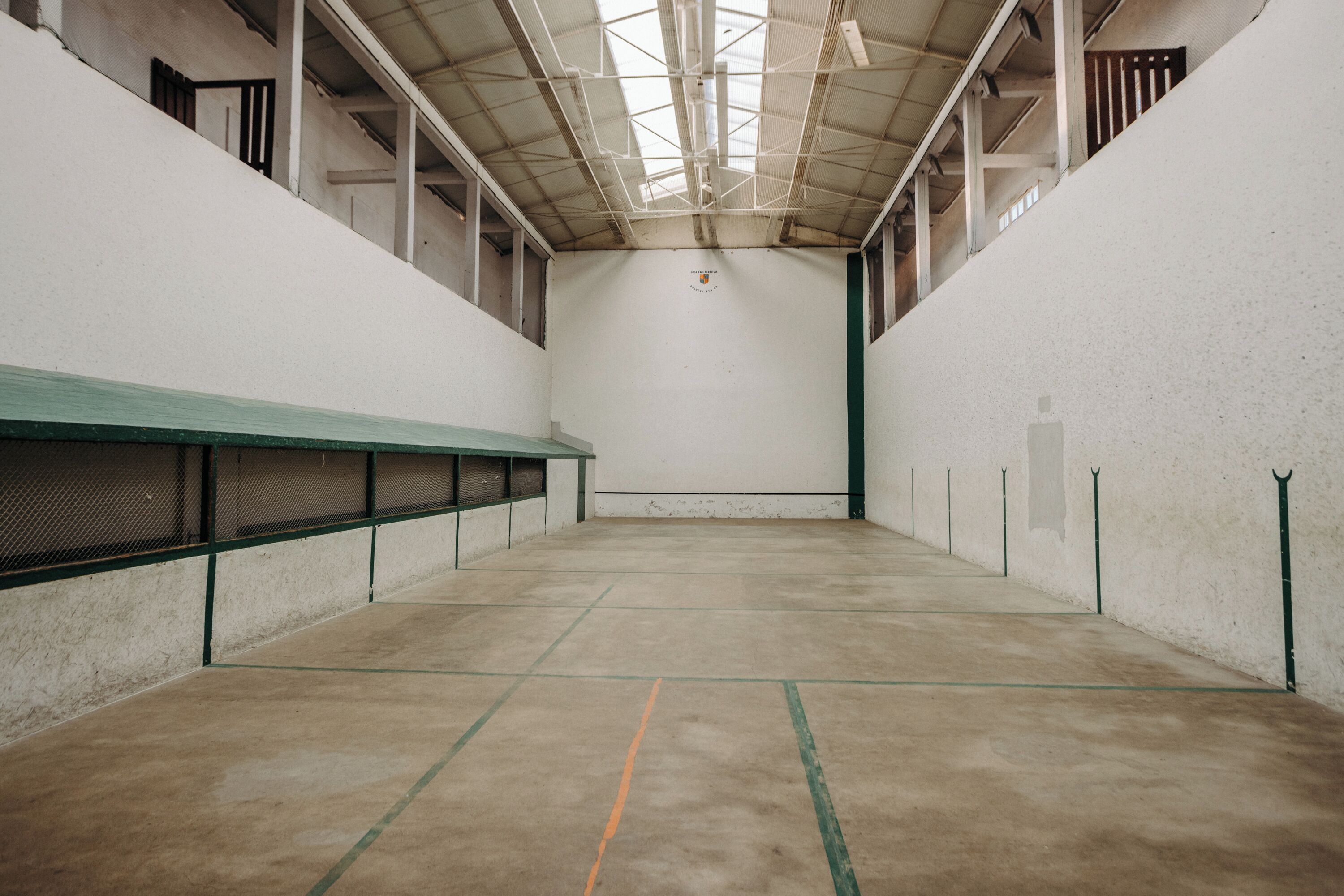 An indoor tennis court with a high ceiling, white walls, and green lines marking the court.