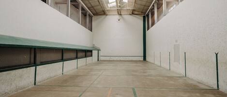 An indoor tennis court with a high ceiling, white walls, and green lines marking the court.