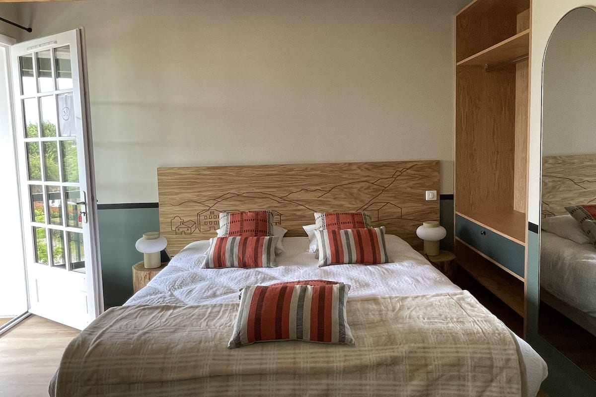 A bedroom with a wooden headboard, a large bed with white bedding and striped pillows, a wooden wardrobe, and a door leading to a balcony.