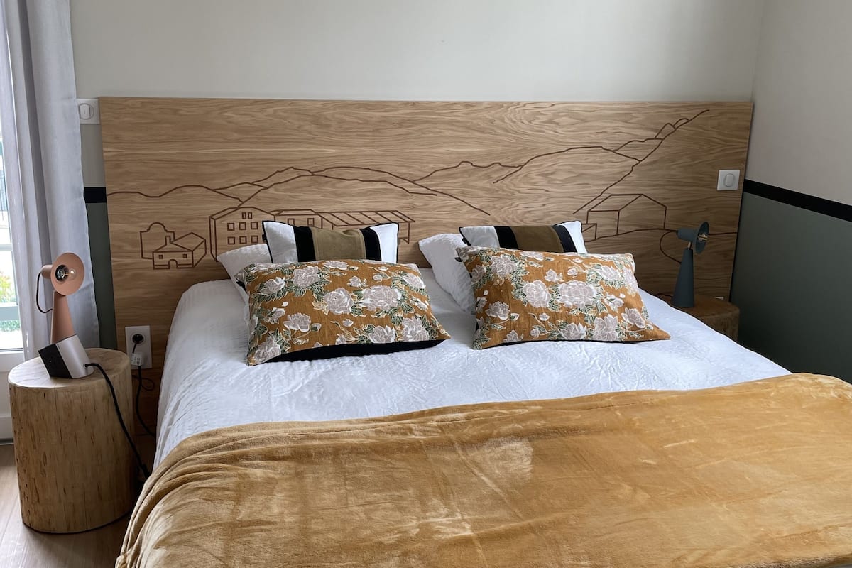 A neatly made bed with a wooden headboard, two floral pillows, and a brown throw blanket.