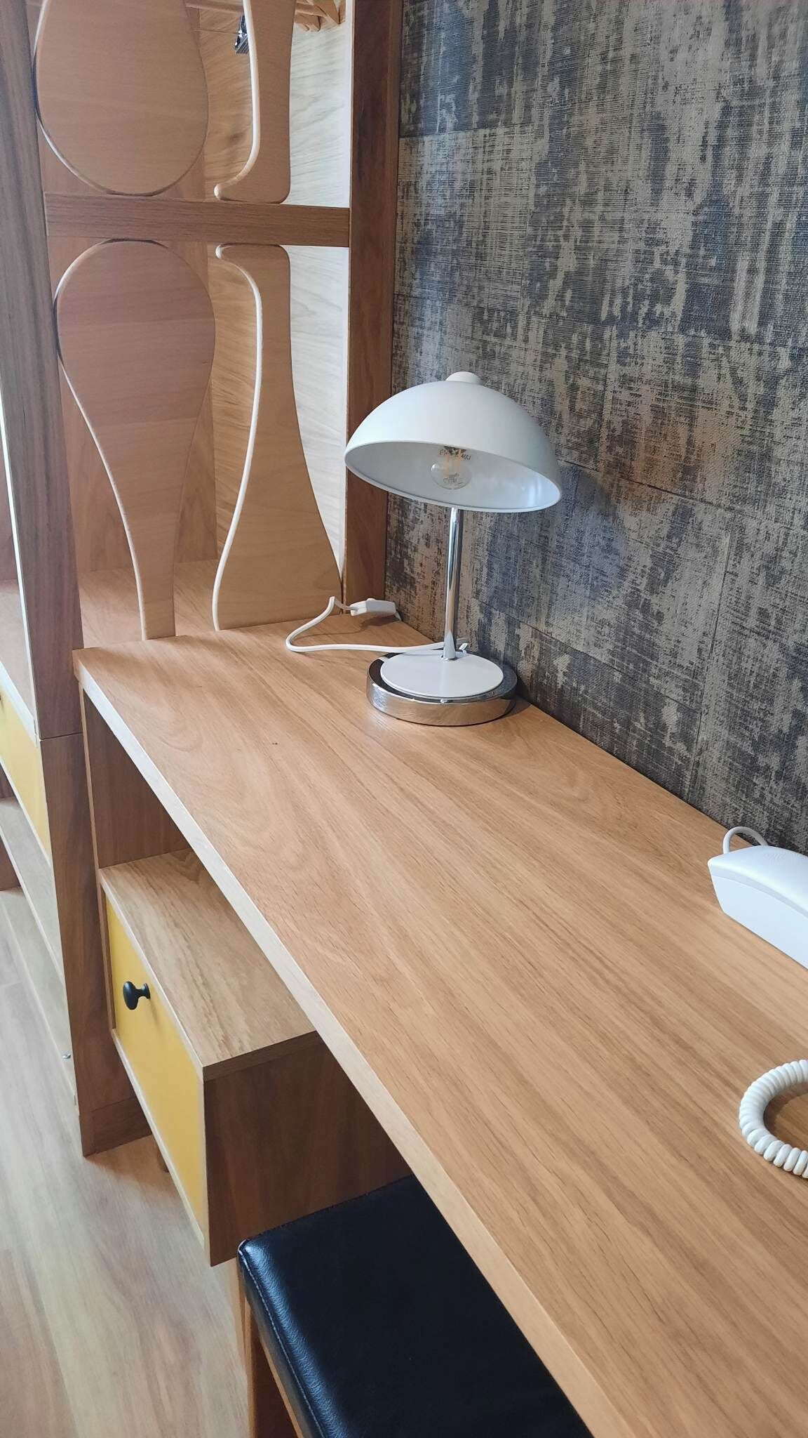 Un escritorio de madera con una lámpara blanca, un teléfono y una cómoda.