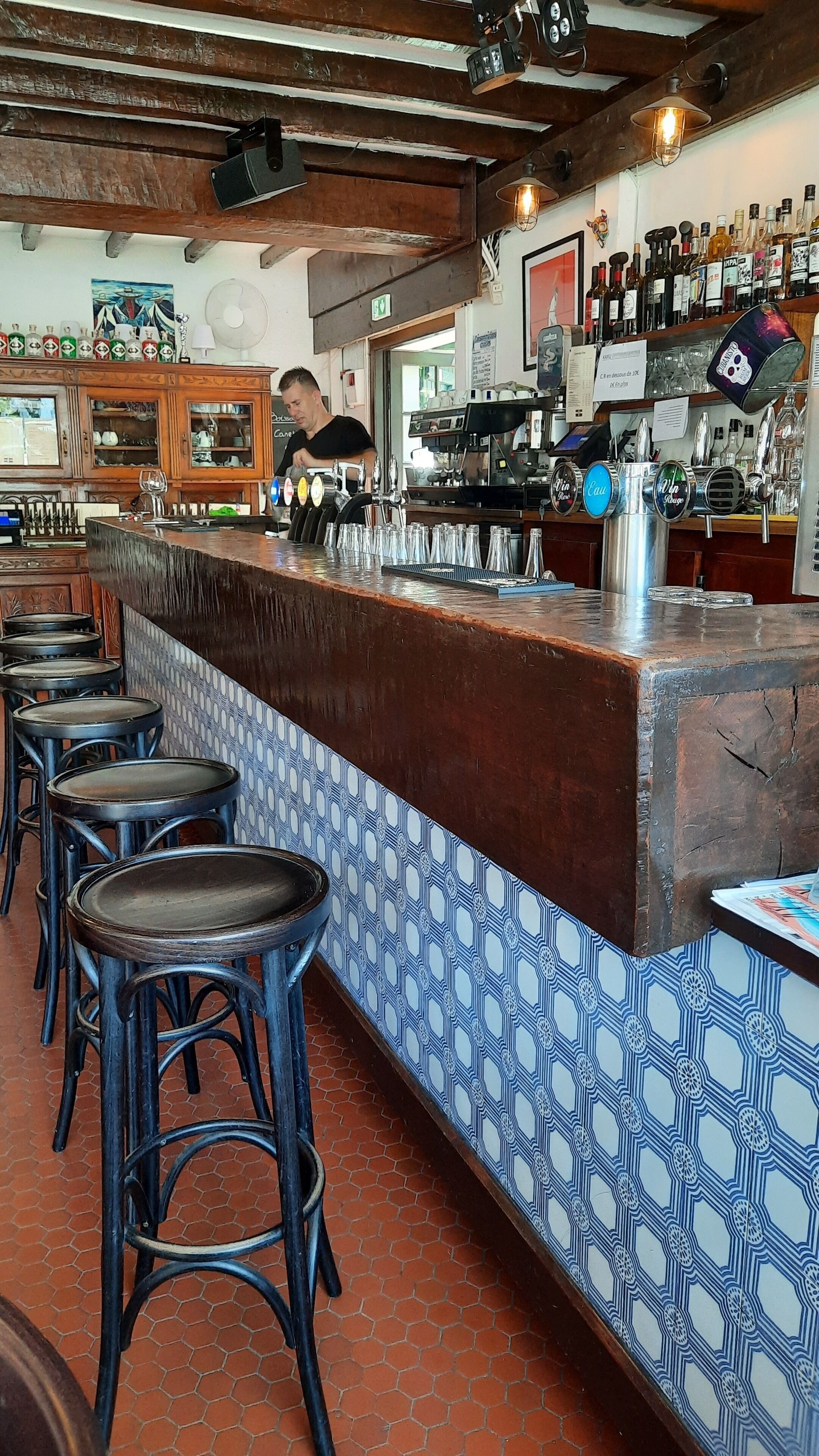 Zona de bar con taburetes, una barra y una variedad de botellas y vasos.