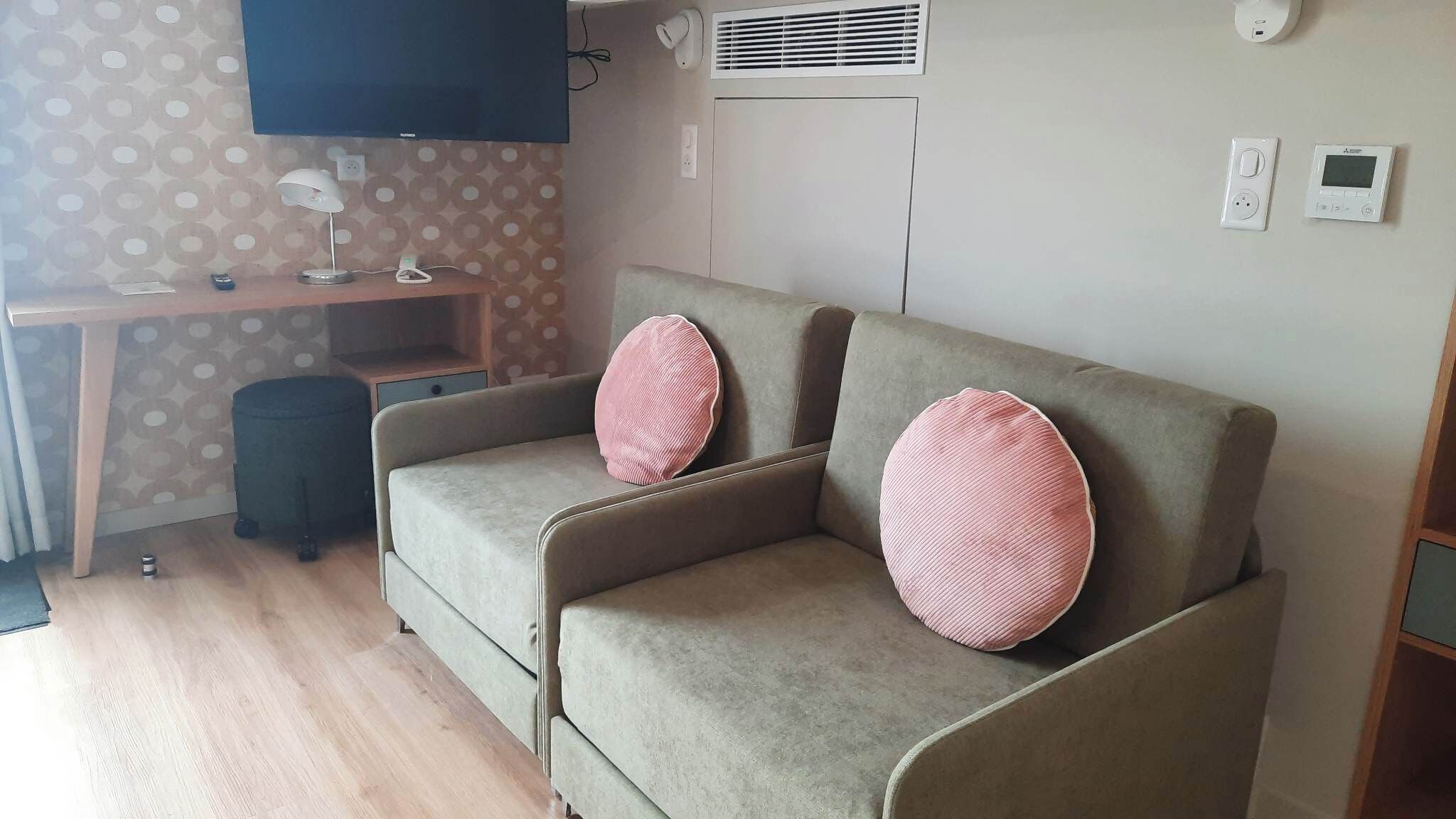 Un espacio habitable compacto con sofá, escritorio pequeño, televisor y aire acondicionado instalado en la pared.