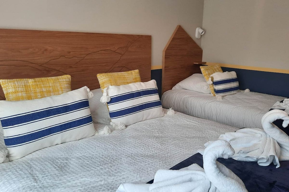 A hotel room with two beds, each with a wooden headboard, white bedding, and striped pillows.