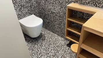 A bathroom with a white toilet, a wooden shelf unit, and a terrazzo floor.