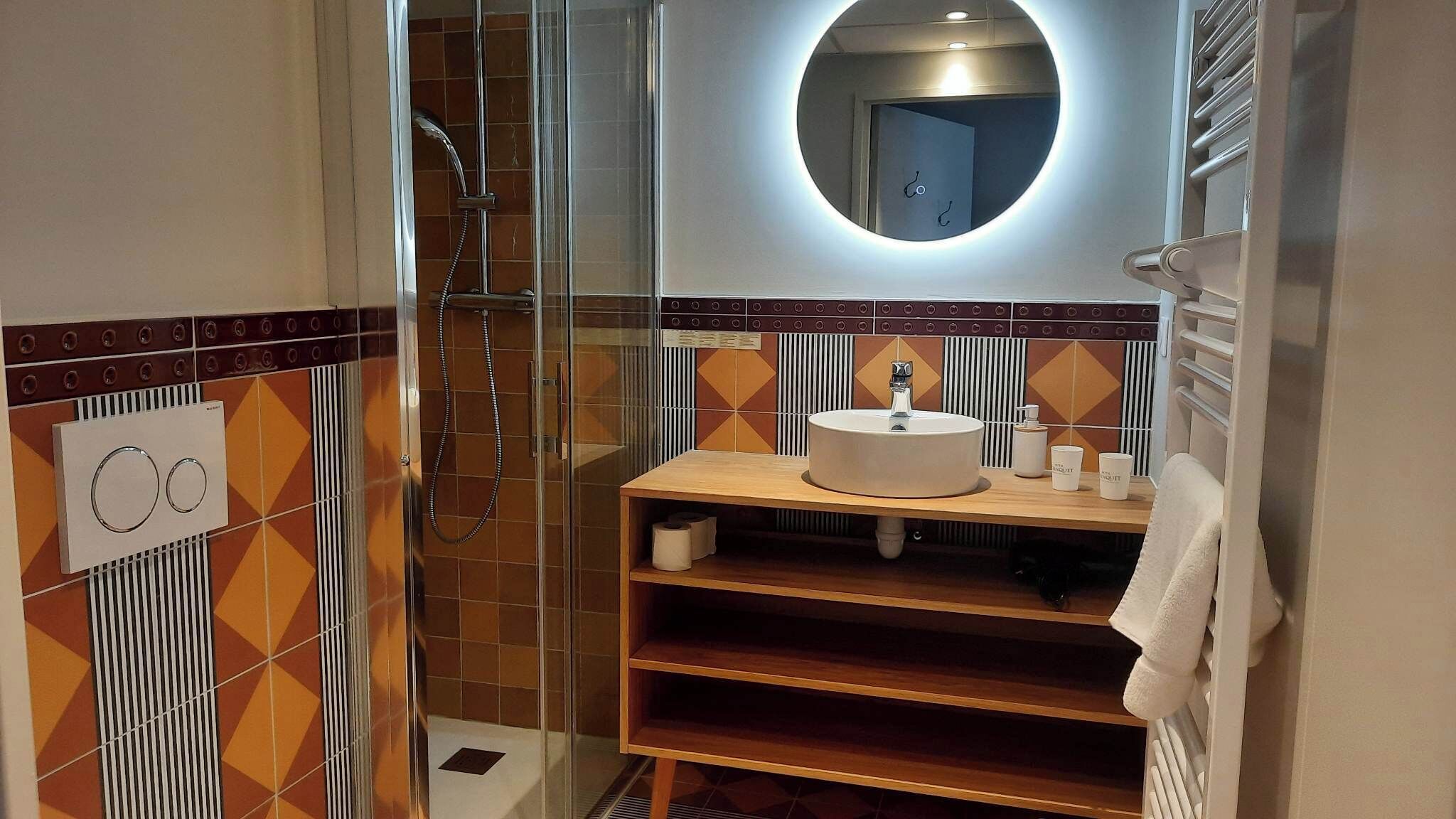 A modern bathroom with a glass shower enclosure, a round mirror, and a wooden vanity with a sink.