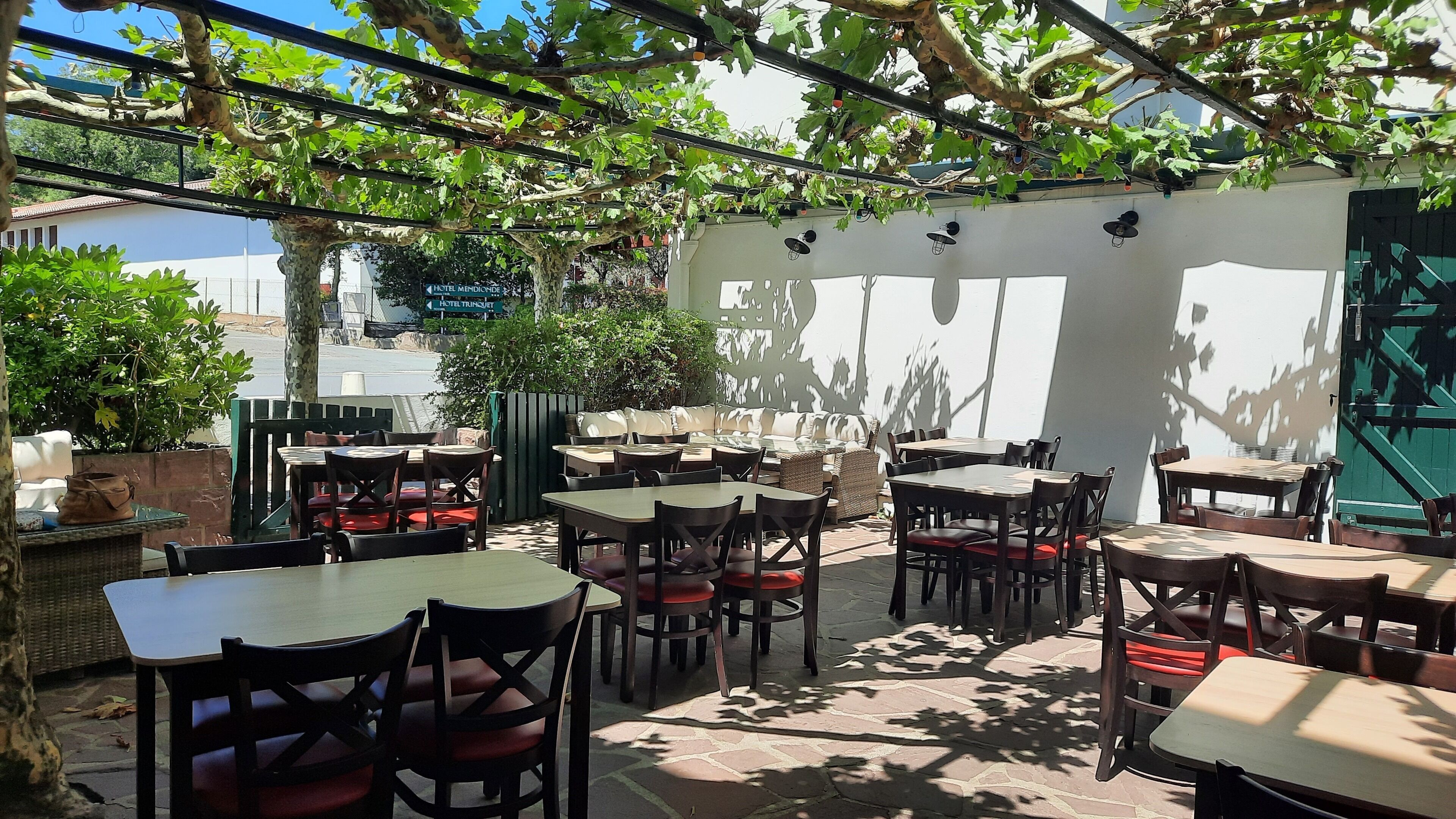 Un espace extérieur aménagé avec des tables et des chaises, entouré de verdure et agrémenté d’une pergola.