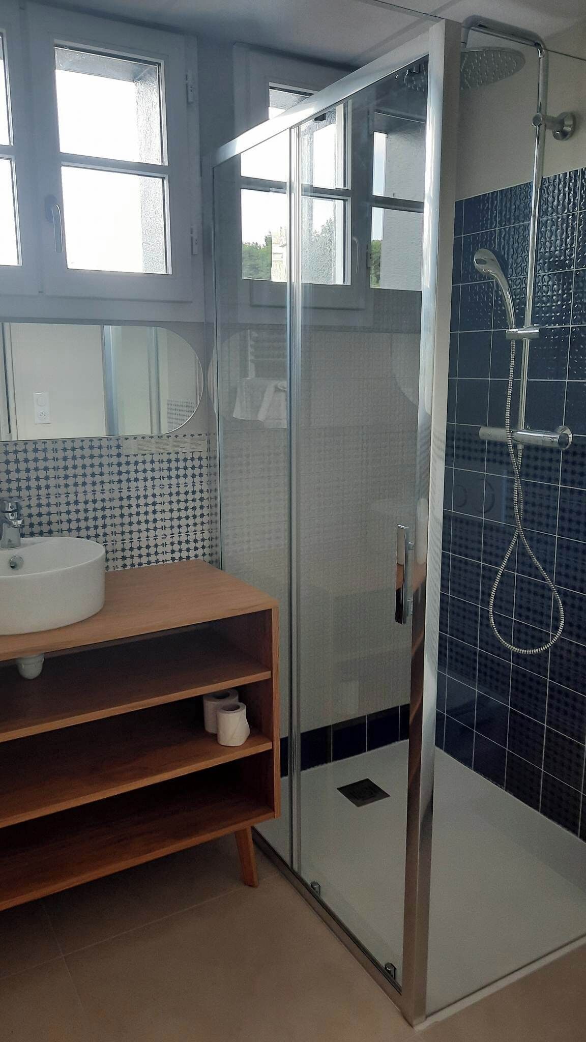 Un baño con cabina de ducha de vidrio, un lavabo con espejo y un estante con artículos de aseo.