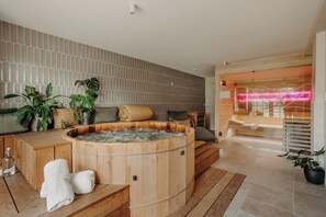 A modern spa area with a wooden hot tub, wooden flooring, and a seating area with cushions. - Hotel Trinquet (Saint-Pee-sur-Nivelle)