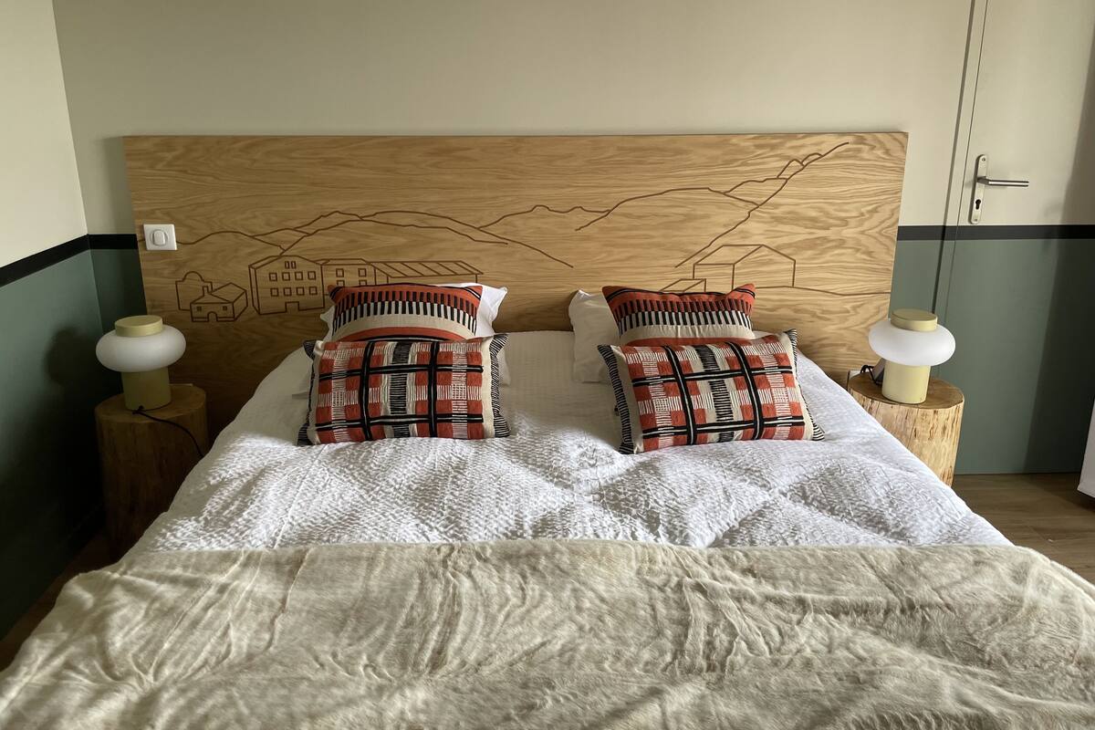 A bed with a wooden headboard, two patterned pillows, and two bedside lamps on wooden stands.