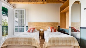 A bedroom with two beds, wooden beams, a large mirror, and a sliding glass door to a balcony. - Hotel Trinquet (Saint-Pee-sur-Nivelle)