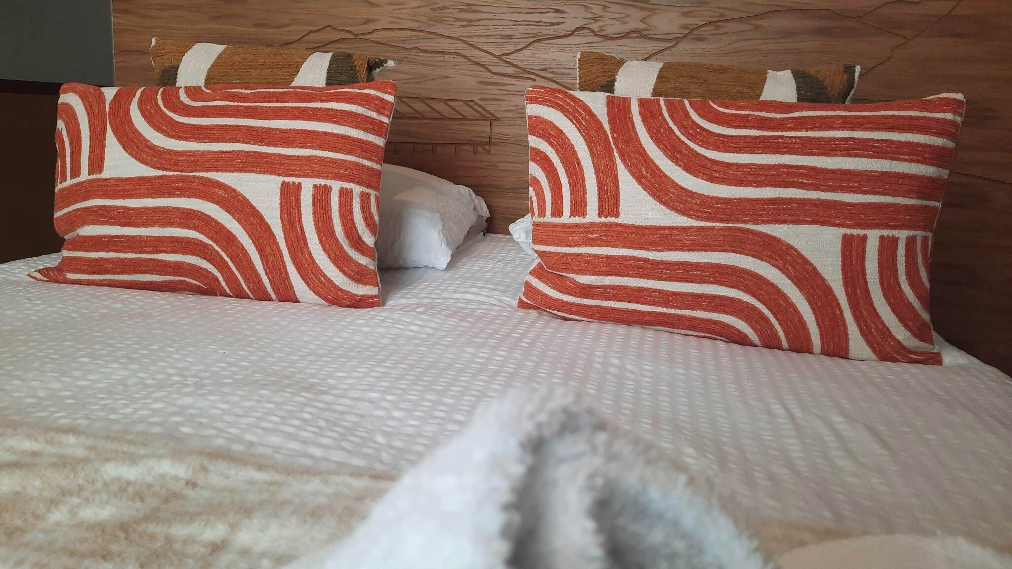 A bed with two pillows featuring a red and white striped pattern, a wooden headboard, and a white textured bedspread.
