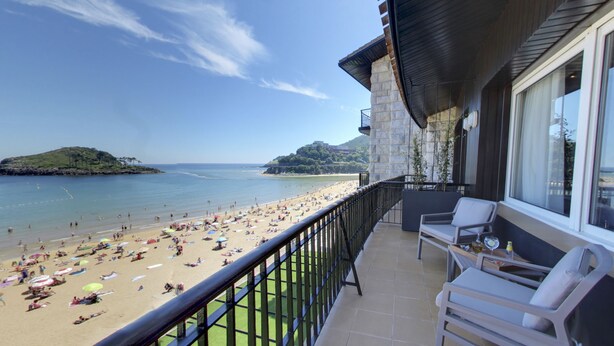 A balcony with a view of a beach and distant hills. - Hotel Silken Palacio Uribarren (Lekeitio)