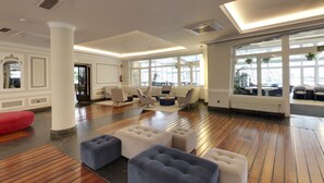 A spacious lobby with wooden flooring, modern seating, large windows, and a red bean bag. - Hotel Silken Palacio Uribarren (Lekeitio)