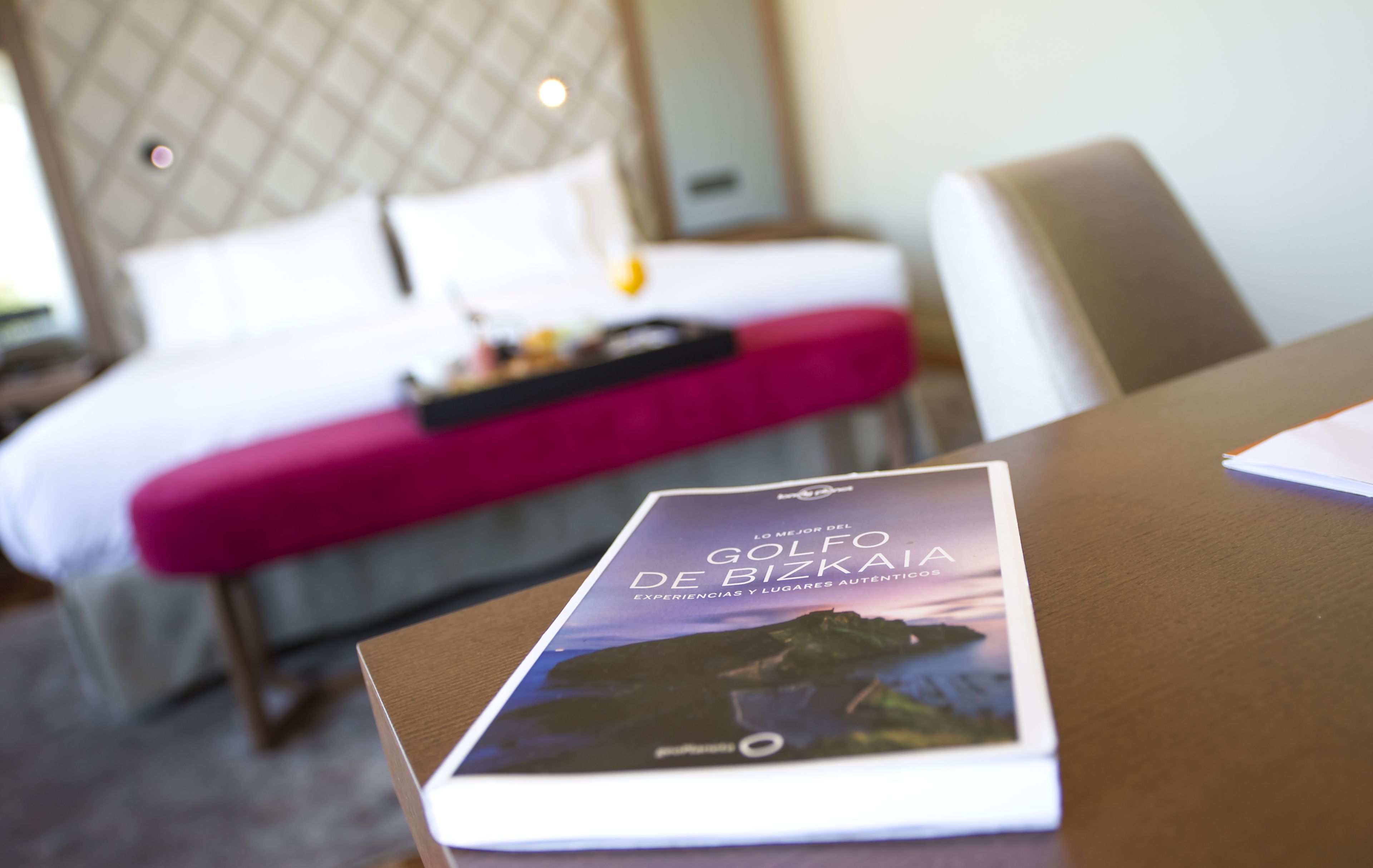A hotel room with a bed, a bedside table with a brochure, and a chair.