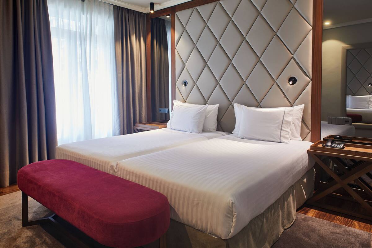 A double bed with a tufted headboard, a red bench, and a bedside table with a phone.