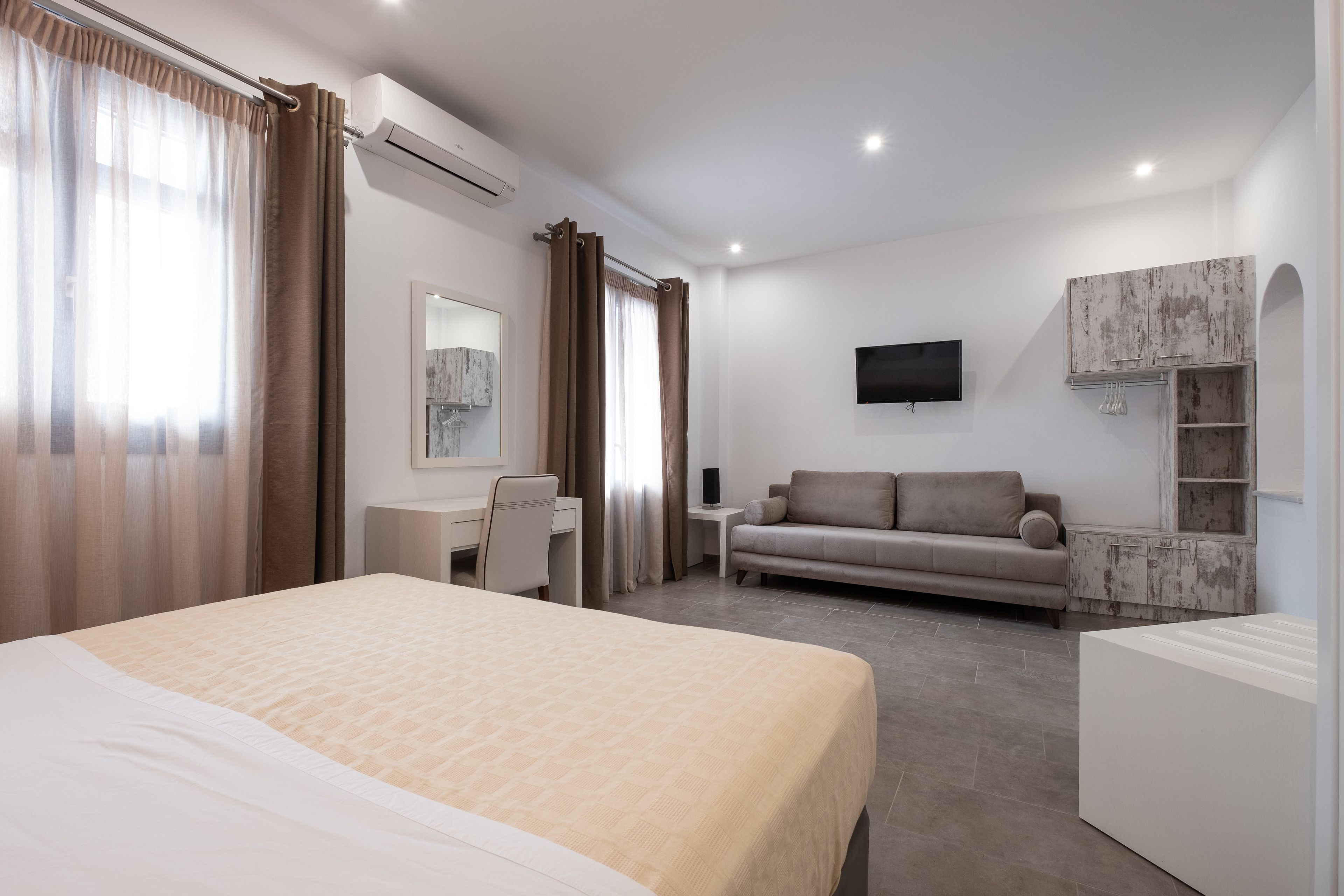 Quarto de hotel moderno com uma cama grande, uma escrivaninha, um sofá e uma televisão na parede.