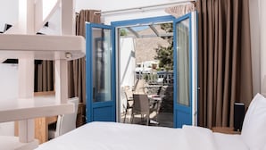 A hotel room with a bed, a desk, and a view of an outdoor terrace with chairs and a table. - Tristhenia Hotel (Santorini)
