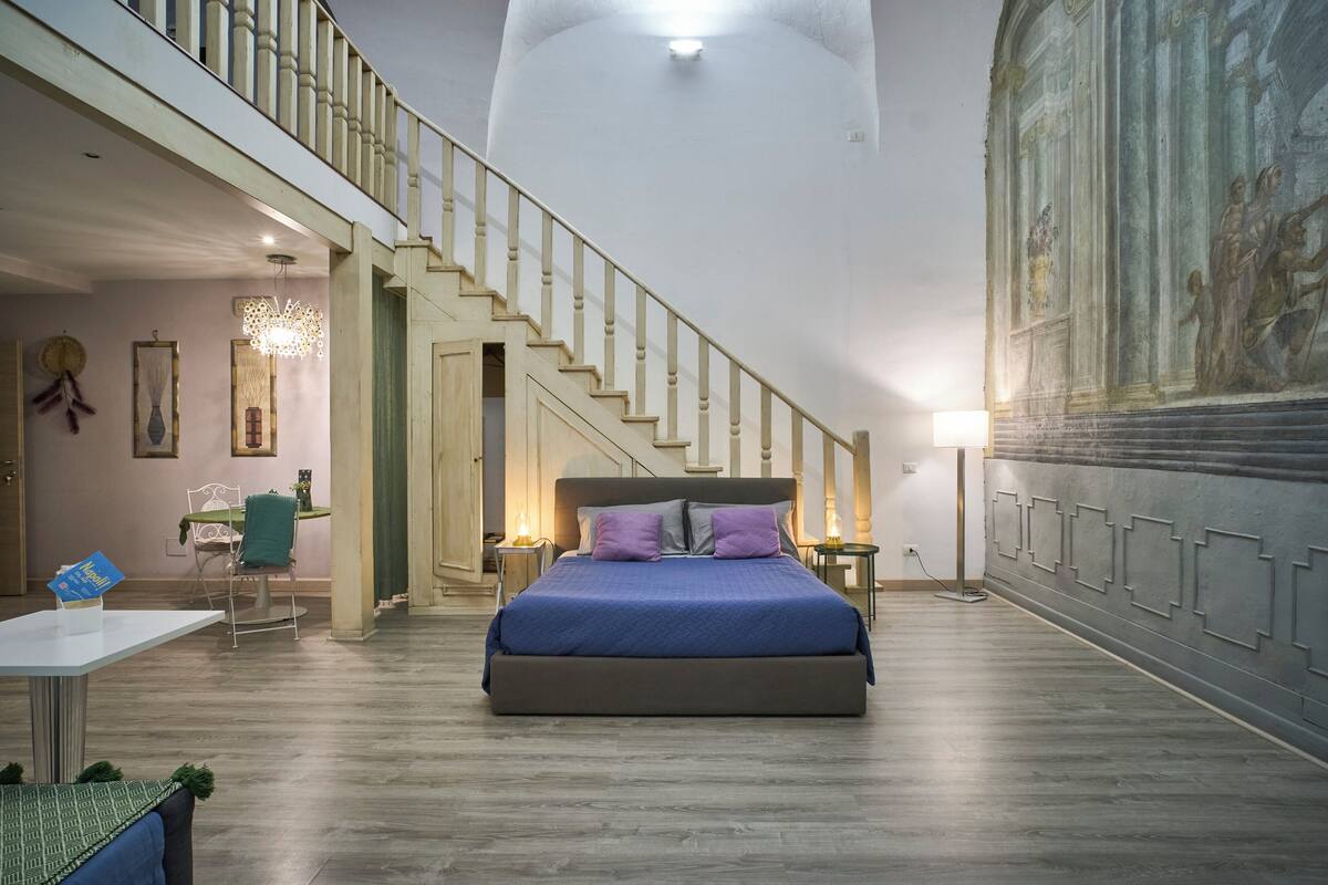 A spacious bedroom with a large bed, a staircase, and a mural on the wall.