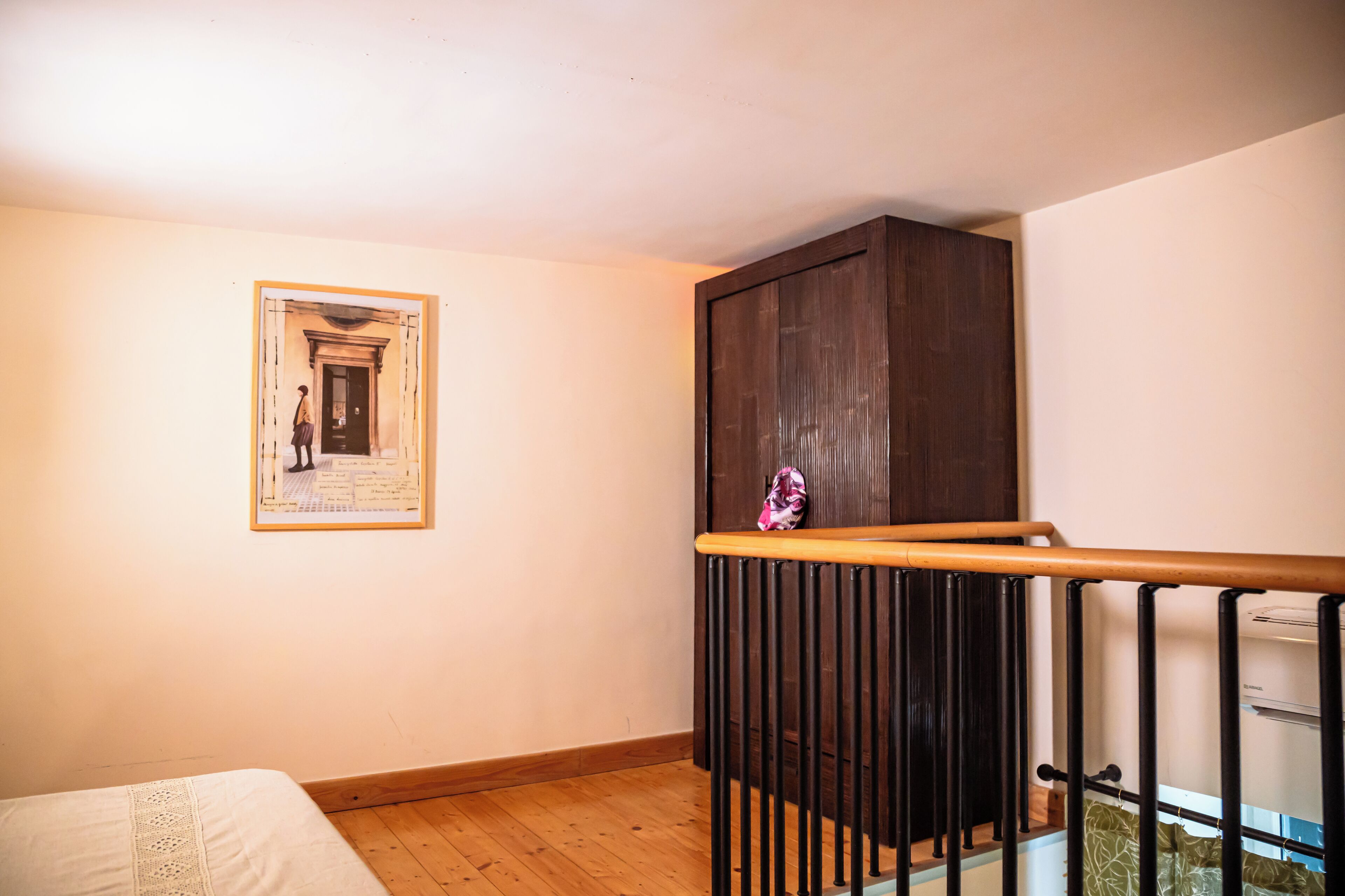 Una habitación con suelo de madera, una cama con colcha blanca, un mueble de madera oscura y un cuadro enmarcado en la pared.