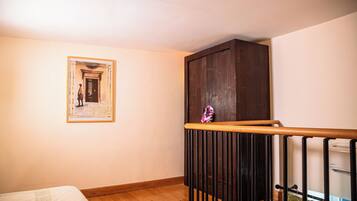 Una habitación con suelo de madera, una cama con colcha blanca, un mueble de madera oscura y un cuadro enmarcado en la pared.